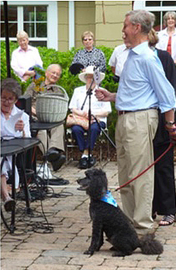 a man with a dog on a leash addresses a small group of people sitting at tables